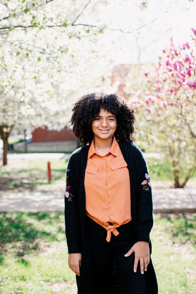 Providence College student posed in front of blooming Spring trees.