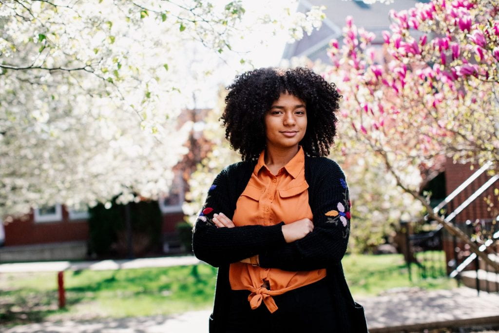 Providence College student posed with arms crossed in front of blooming Spring trees.
